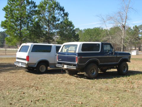 1978 Ford Bronco - Photo of a white Ford and a dark vintage Bronco rear view in a field, not a technical document.
