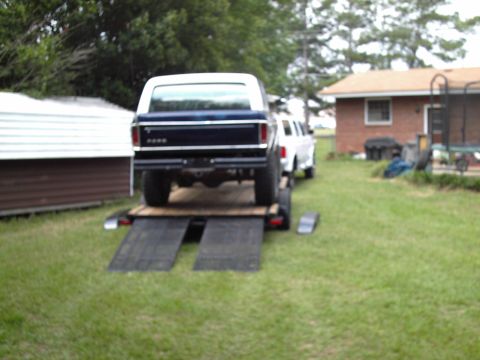1978 Ford Bronco - A dark-colored truck is positioned on ramps, ready to be loaded onto a trailer in a grassy area.