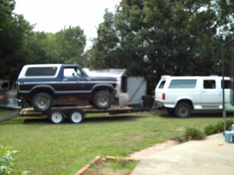 1978 Ford Bronco - A blue and white 1978 Ford Bronco is loaded onto a trailer, with a white SUV parked behind it.