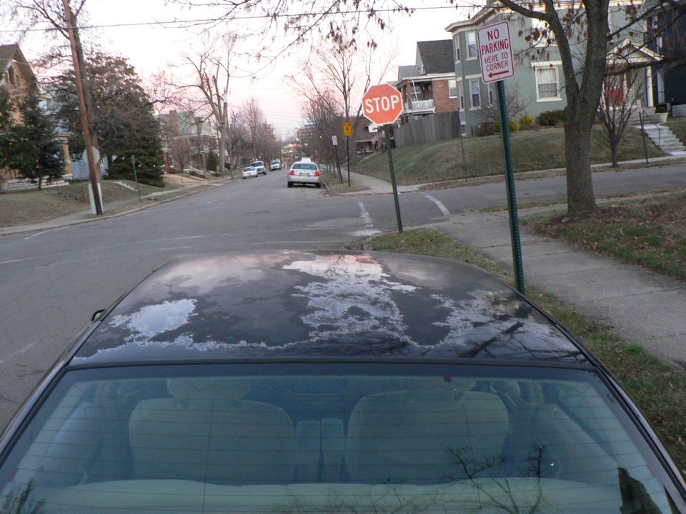 Dark green sedan roof and rear glass with frost patches at a stop sign corner