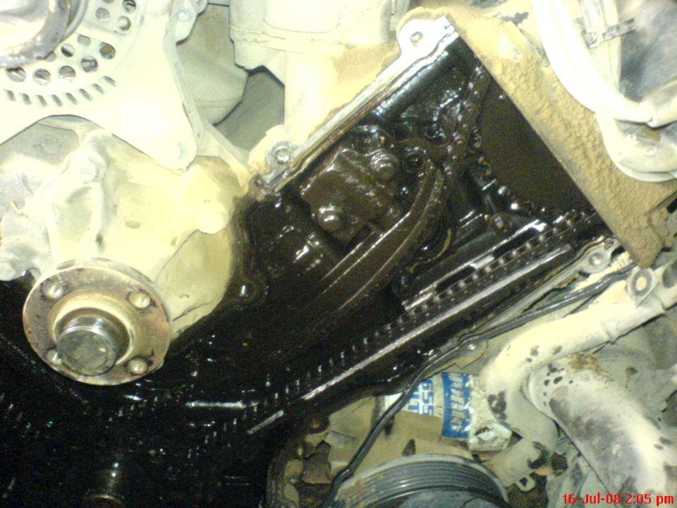 Close-up of a dirty vehicle engine's timing chain and gears covered in oil.