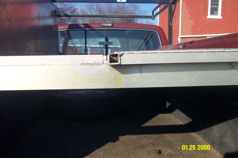 Close-up of flatbed truck side, showing pickup cab rear window and spare tire underneath.