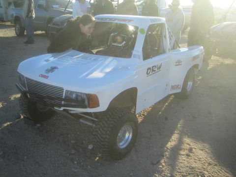 1990 Ford Bronco - Photograph of a white tube-chassis off-road race truck being prepped in a desert pit area, not a technical document.