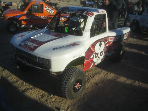 1990 Ford Bronco - Photograph of a white and red off-road race truck with skull graphics parked in a desert pit, not a technical document.