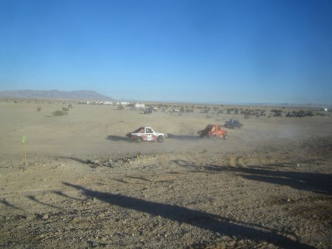 1990 Ford Bronco - Photograph of two off-road race trucks racing across open desert, not a technical document.