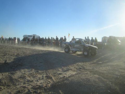 1990 Ford Bronco - Photograph of an off-road race truck driving a dusty desert course beside a crowd, not a technical document.