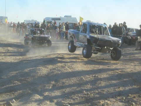 1990 Ford Bronco - Photograph of off-road race trucks launching off the start line in a desert race, not a technical document.