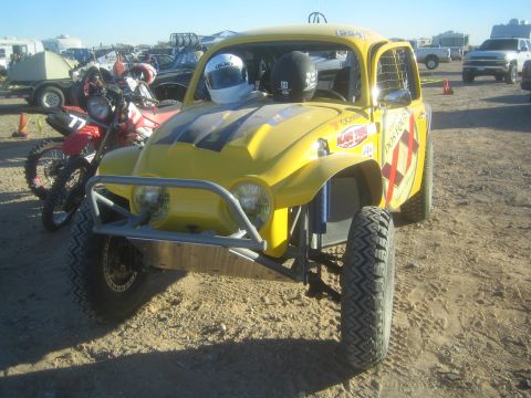 1990 Ford Bronco - Photograph of a yellow Baja Bug off-road race car parked in a desert pit beside dirt bikes, not a technical document.