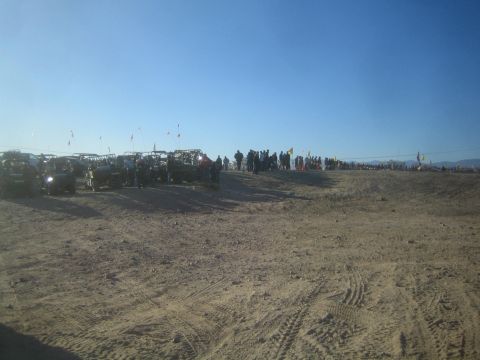 1990 Ford Bronco - Photograph of a distant row of off-road vehicles and spectators across a desert plain, not a technical document.