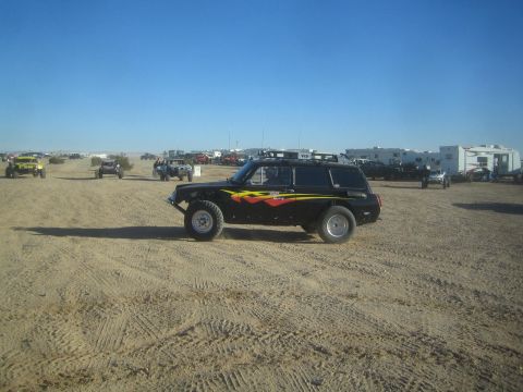 1990 Ford Bronco - Photograph of a black off-road race station wagon parked in a desert staging area with RVs, not a technical document.