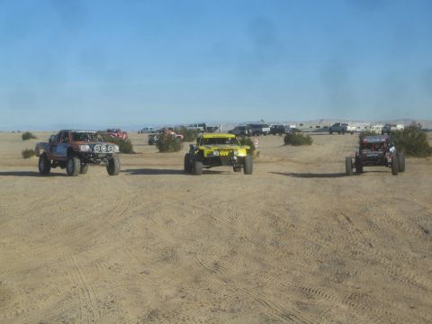 1990 Ford Bronco - Photograph of three off-road race vehicles staged across an open desert course, not a technical document.