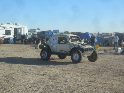 1990 Ford Bronco - Photograph of a tan Baja Bug race car number 591 in a desert pit area, not a technical document.