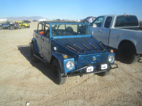 1990 Ford Bronco - blue Volkswagen Thing with a roll bar, roof rack and tubular bumpers parked on dirt next to a silver pickup truck.