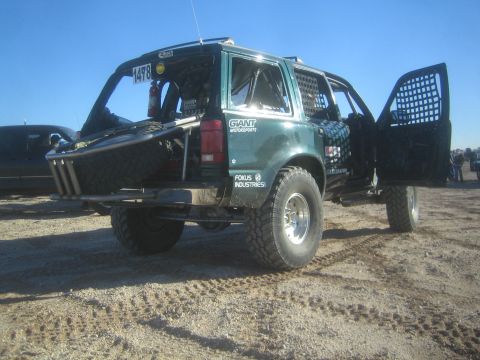 1990 Ford Bronco - rear three-quarter view of a green number 1478 race SUV with an open rear door, mesh window covers and a tubular bumper on dirt.