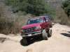 1996 Ford Bronco - A red Ford Bronco navigates a dusty, off-road trail surrounded by dry brush and trees.