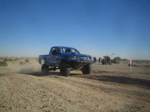 1990 Ford Bronco - Photo of a blue Ford off-road race truck in the desert, not a technical document.
