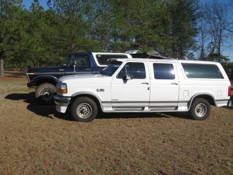 1978 Ford Bronco - Photograph of a white Ford crew-cab pickup beside a vintage Ford Bronco in a yard, not a technical document.