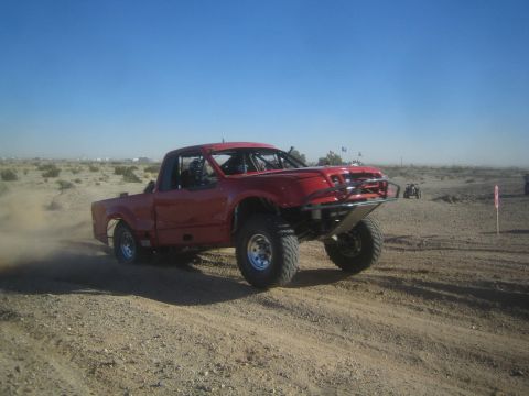 1990 Ford Bronco - Photo of a red off-road race truck on a desert course, not a technical document.