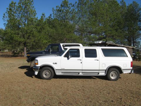 1978 Ford Bronco - Photograph of a white Ford crew-cab pickup and a dark vintage Bronco in a grassy lot, not a technical document.