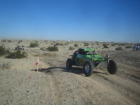 1990 Ford Bronco - Photograph of a green off-road race buggy on a marked desert course, not a technical document.