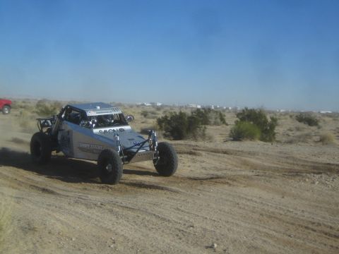 1990 Ford Bronco - Photograph of a silver off-road race buggy on a desert course, not a technical document.