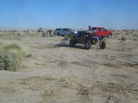 1990 Ford Bronco - Photograph of a dark off-road race truck in the desert, not a technical document.