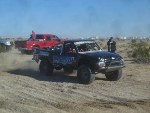 1990 Ford Bronco - Photograph of a black off-road race truck in the desert, not a technical document.