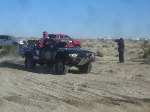 1990 Ford Bronco - Photograph of a black off-road race truck in the desert, not a technical document.