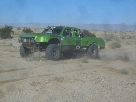 1990 Ford Bronco - Photograph of a green off-road race truck in the desert, not a technical document.
