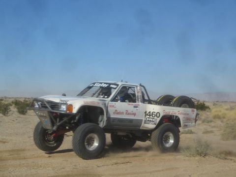 1990 Ford Bronco - Photograph of a white Slater Racing off-road race truck, number 1460, kicking up dust on a desert course.