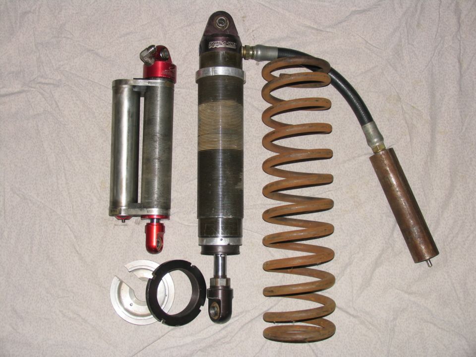 Two shock absorbers and a coil spring on a white textured background.