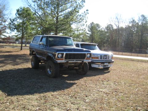 1978 Ford Bronco - Photograph of a blue vintage Bronco and a white Ford pickup in a grassy lot, not a technical document.