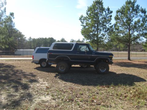 1978 Ford Bronco - Side photograph of a lifted blue vintage Ford Bronco in a yard, not a technical document.