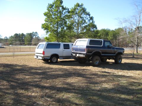 1978 Ford Bronco - Photograph of a lifted blue Ford Bronco and a white pickup from the rear, not a technical document.