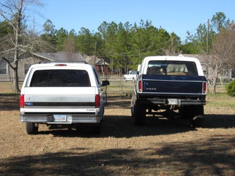 1978 Ford Bronco - Rear-end photograph of a white and a dark Ford pickup in a yard, not a technical document.
