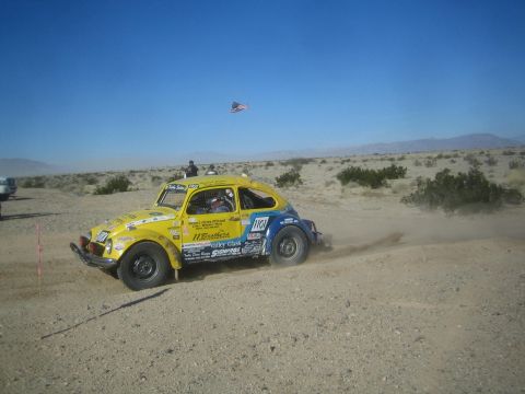 1990 Ford Bronco - Photograph of a yellow Volkswagen Baja Bug race car throwing up dust on a desert course under a flag.