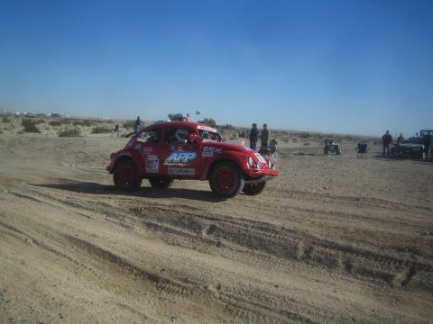1990 Ford Bronco - Photograph of a red APP Racing Volkswagen Baja Bug race car on a sandy desert course with spectators behind.