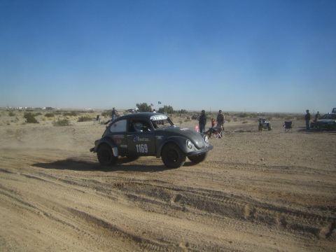 1990 Ford Bronco - Photograph of a grey Volkswagen Baja Bug race car, number 1169, driving across a flat desert course with spectators.