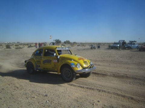1990 Ford Bronco - Photograph of a yellow Volkswagen Baja Bug race car on a desert course with other vehicles in the background.