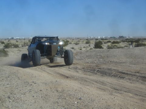 1990 Ford Bronco - Photograph of a single-seat tube-frame off-road race buggy kicking up dust on a flat desert course.