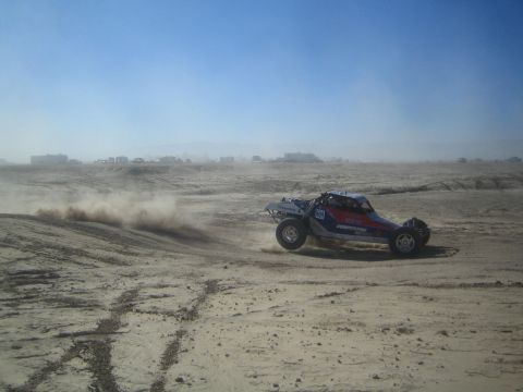 1990 Ford Bronco - Photograph of an open tube-frame off-road race buggy sliding across a dusty desert flat.