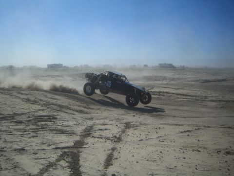 1990 Ford Bronco - Photograph of a dark single-seat off-road race buggy racing across a sandy desert section.