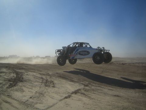 1990 Ford Bronco - Photograph of a white and blue tube-frame off-road race buggy catching air over a desert jump.