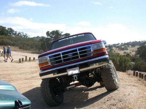 1996 Ford Bronco - This red 1996 Ford Bronco is shown in a 3/4 front view on a dirt road, likely during an off-road excursion.