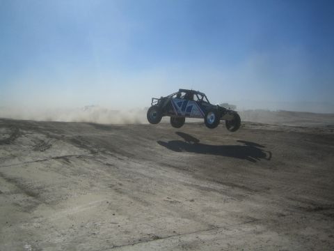 1990 Ford Bronco - Action photo of a tube-frame off-road buggy catching air on a dirt course, not a technical document.