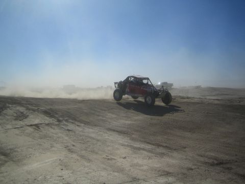 1990 Ford Bronco - Action photo of a red tube-frame off-road buggy airborne on a desert track, not a technical document.