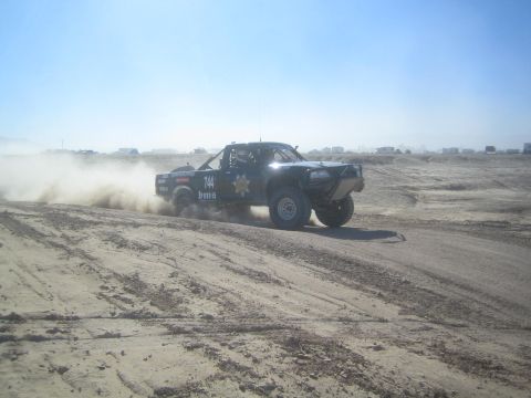 1990 Ford Bronco - Action photo of an off-road prerunner truck sliding on a desert course, not a technical document.