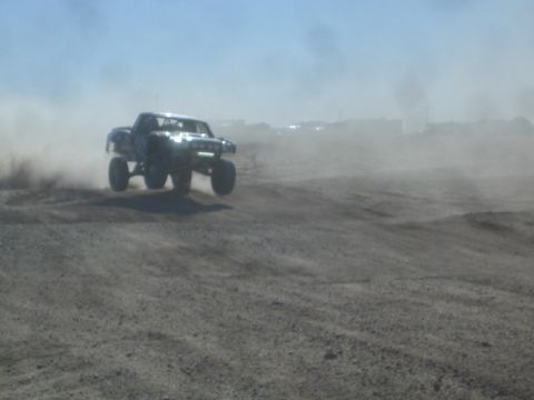 1990 Ford Bronco - Action photo of an off-road prerunner truck catching air in the desert, not a technical document.