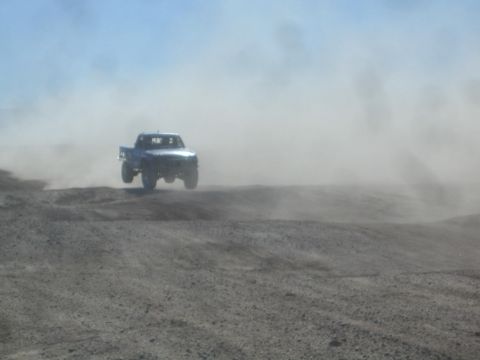 1990 Ford Bronco - Action photo of a blue off-road truck airborne on a desert course, not a technical document.