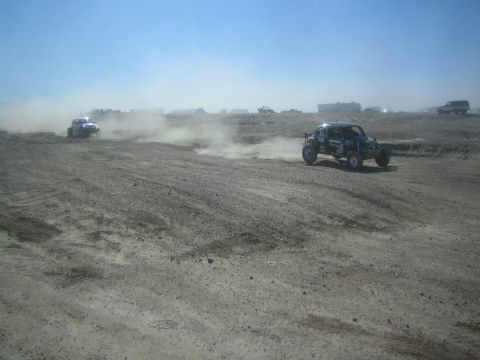 1990 Ford Bronco - Action photo of two off-road buggies racing across an open desert flat, not a technical document.